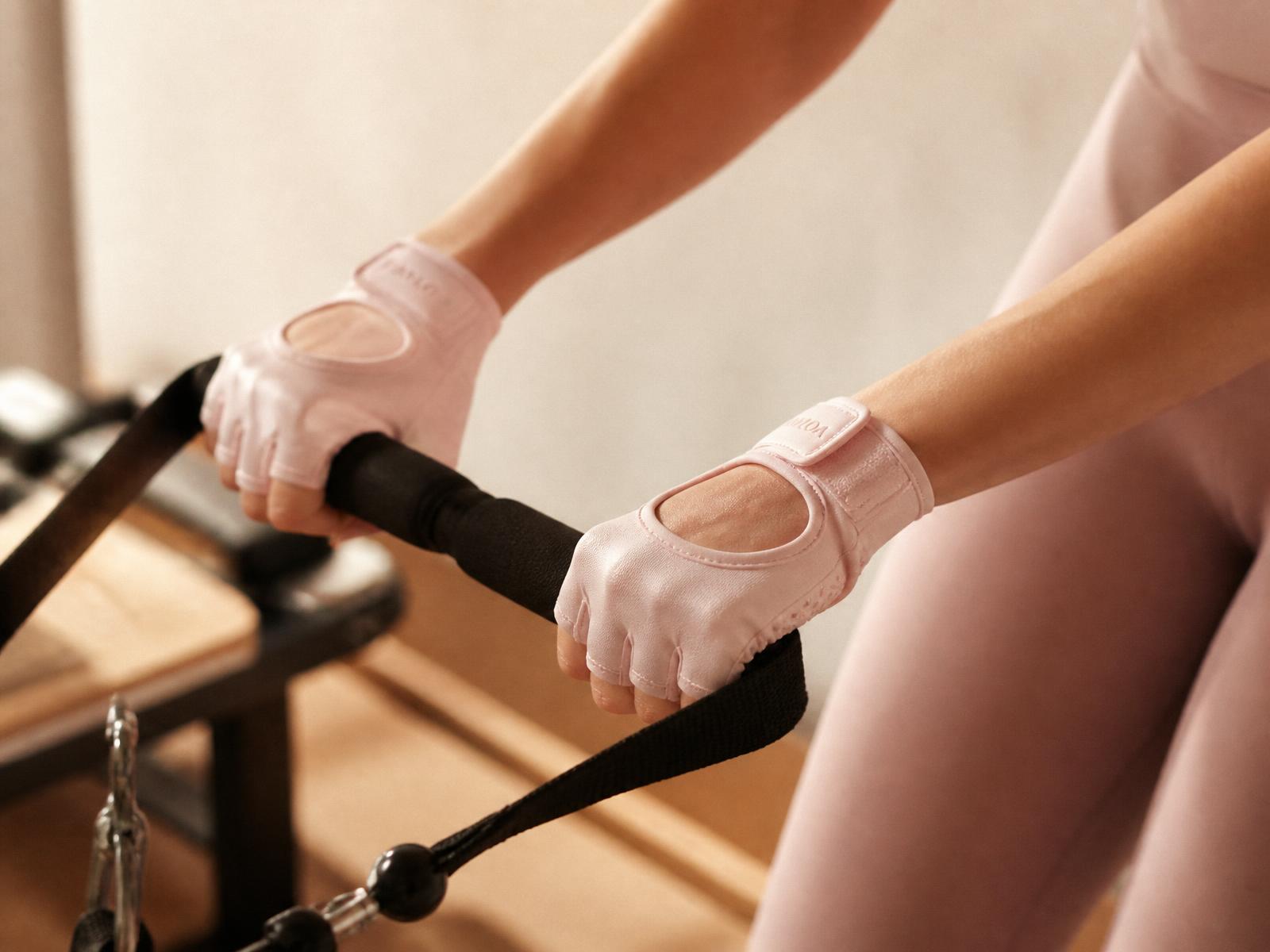 Hands wearing blush Lyssara Pilates grip gloves holding a reformer strap handle